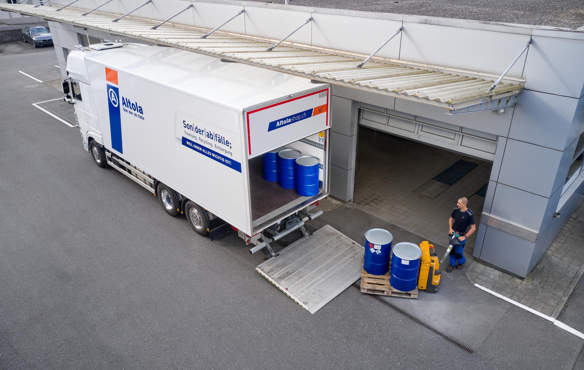 Drohnenaufnahme eines Altola-Mitarbeiters. Er belädt einen weissen LKW mit blauen Metallfässer.